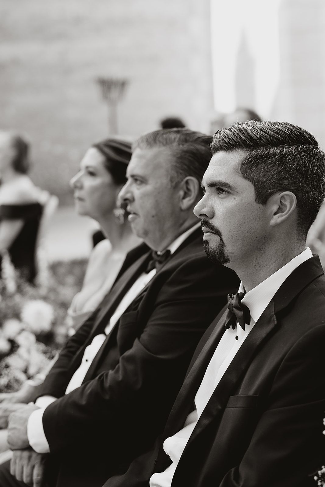 Wedding guests in formal attire seated at reception watching ceremony.