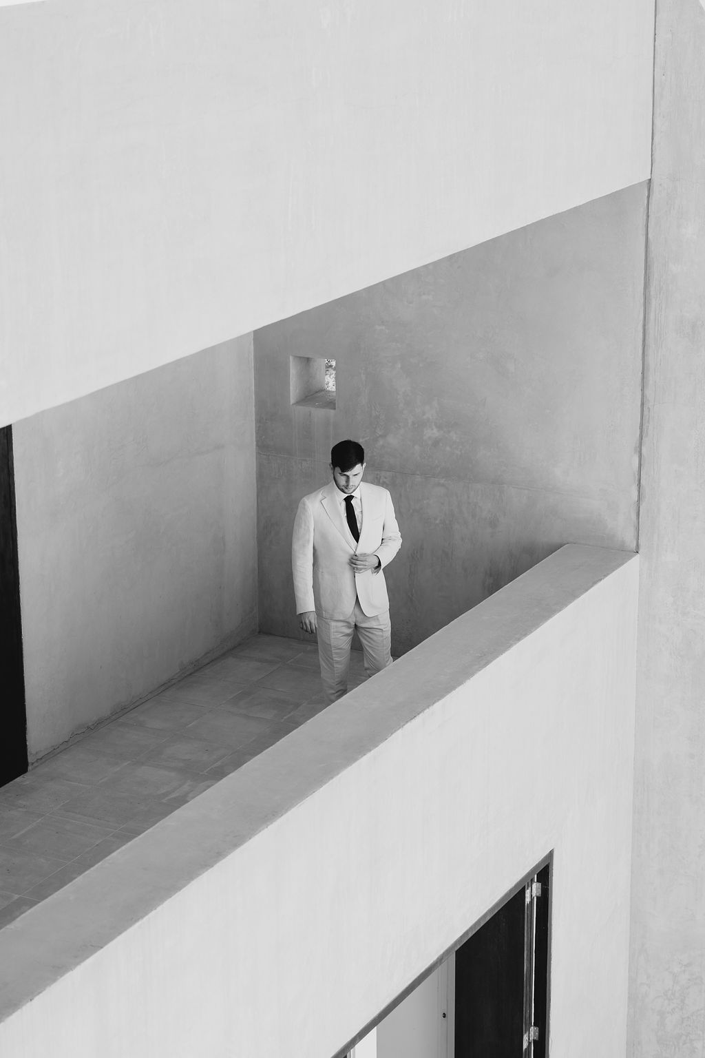 Person in white suit standing in geometric architectural space, black and white photo.