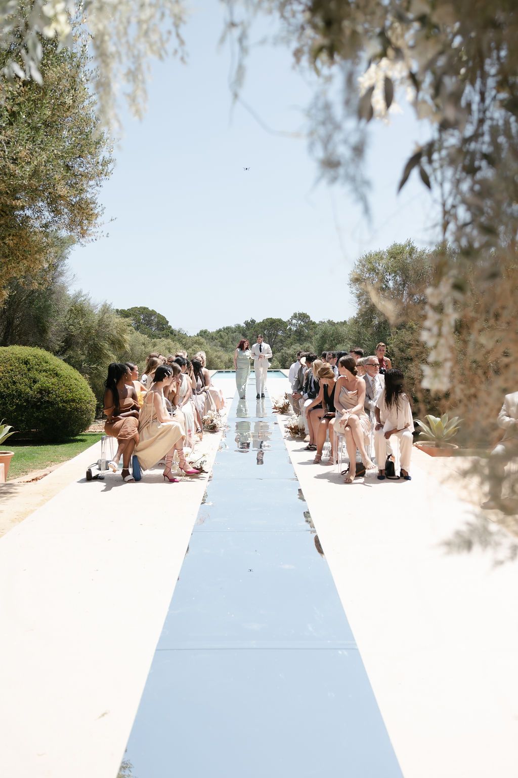 Outdoor wedding ceremony with guests seated along a reflective white aisle runner.