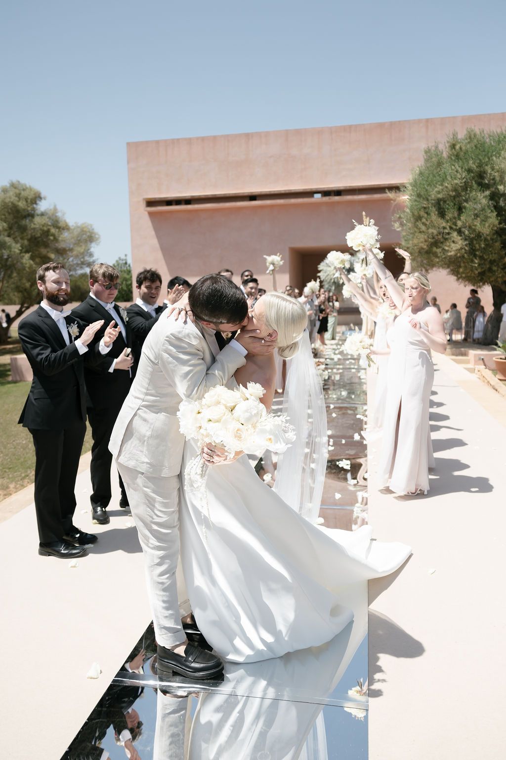 Wedding guests gather around a mirrored aisle at an outdoor ceremony venue.