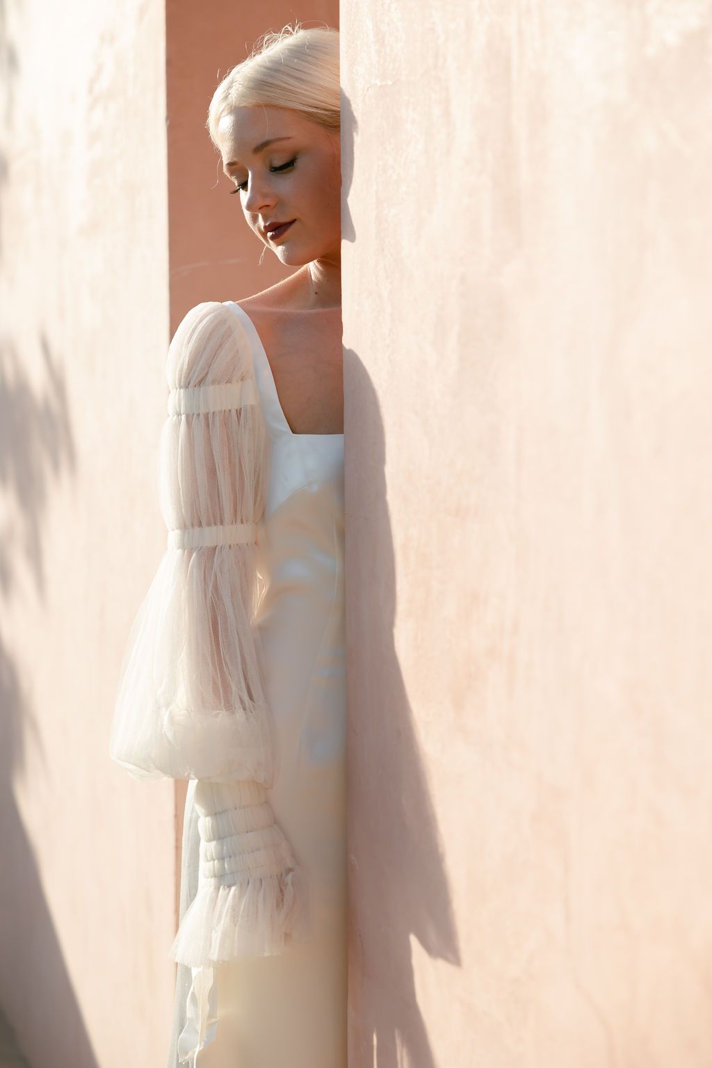 Dreamy bridal fashion shot featuring sheer balloon sleeves and structured bodice against peach wall.