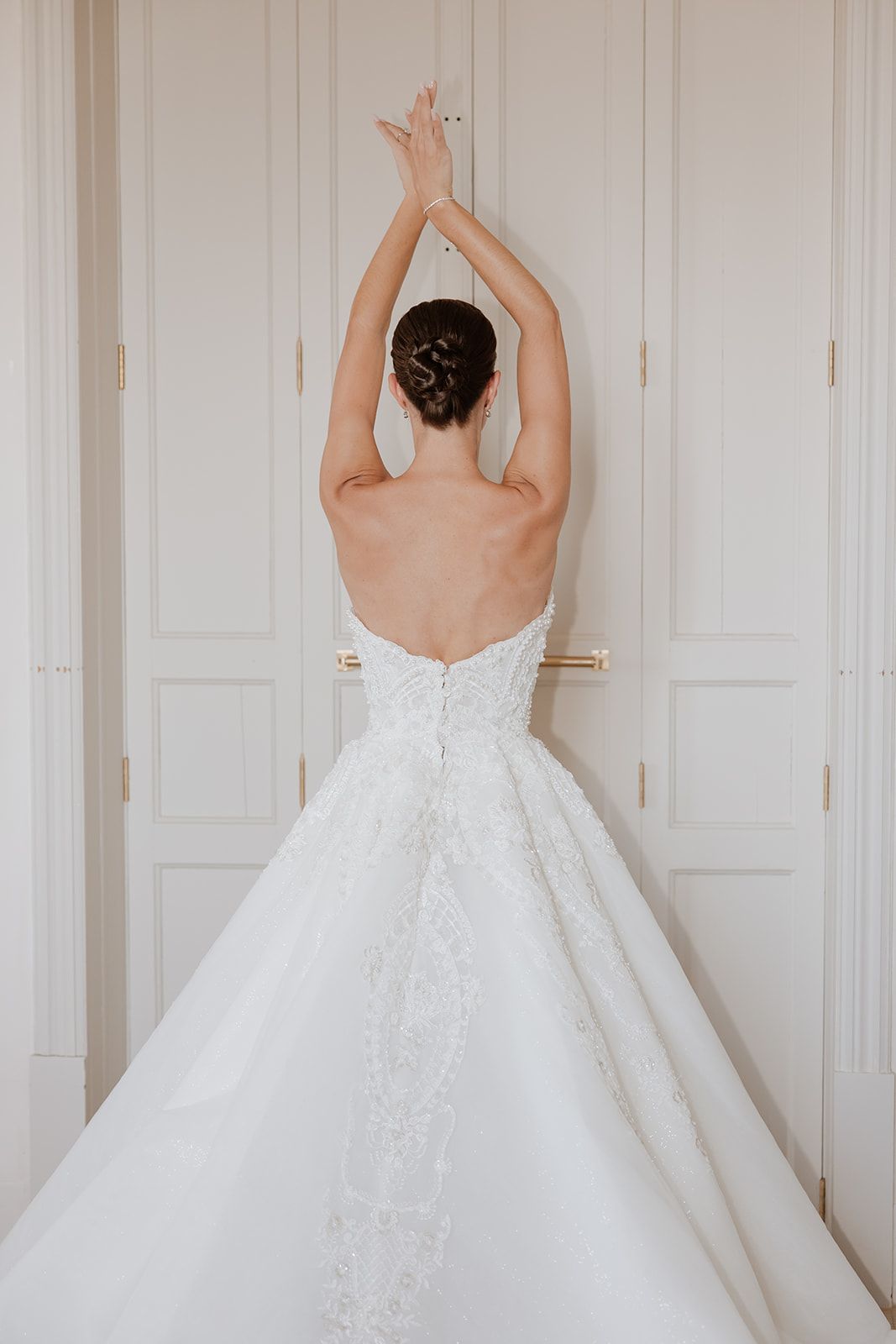 Back view of bride in lace wedding dress with arms raised gracefully.