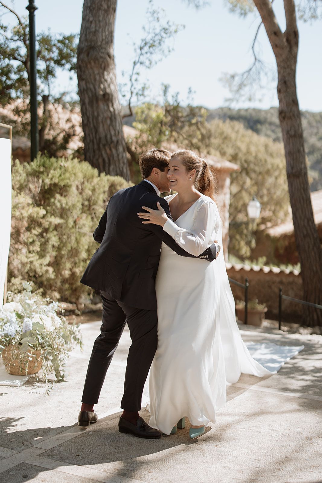Couple in wedding attire share intimate moments in sun-dappled outdoor setting.