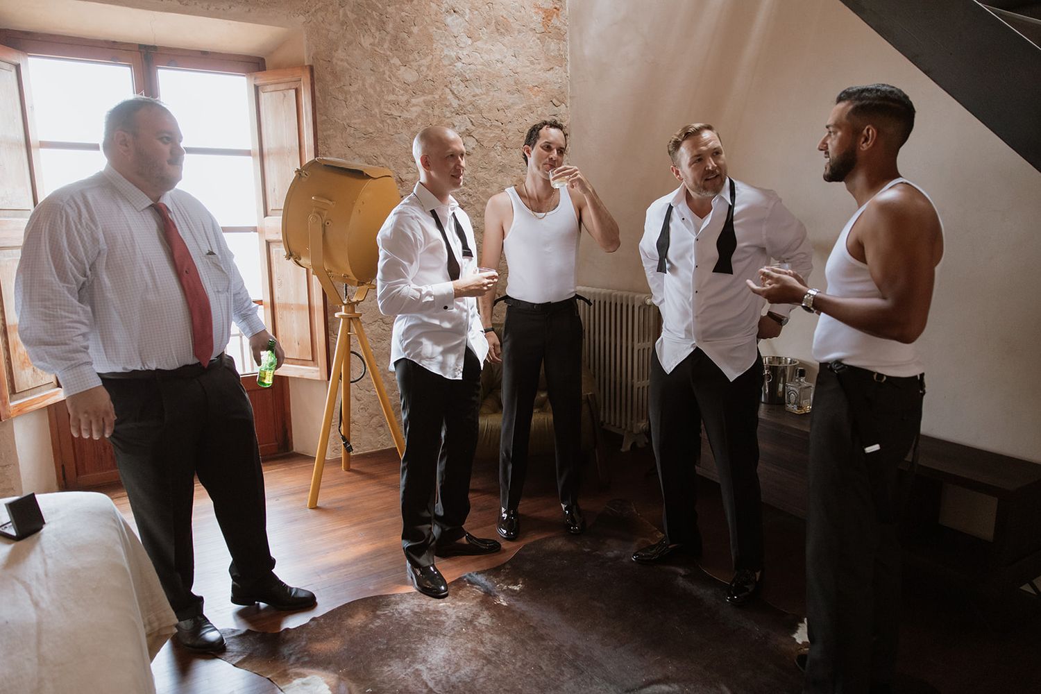 Group of people in formal attire gathering and talking in rustic indoor setting.