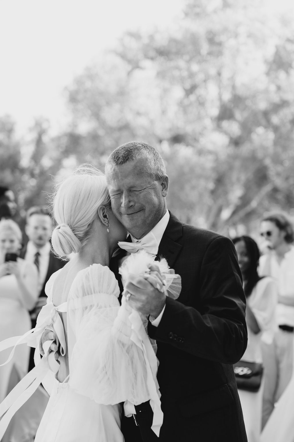A tender black and white moment during a wedding dance with guests watching.