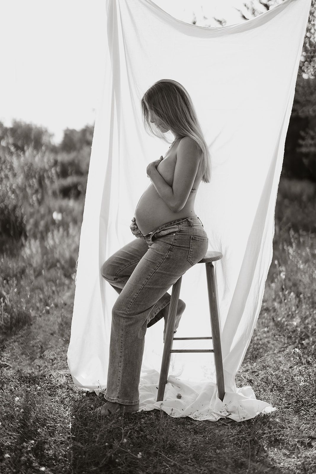 Side profile maternity portrait in black and white against outdoor setting with white fabric backdrop.