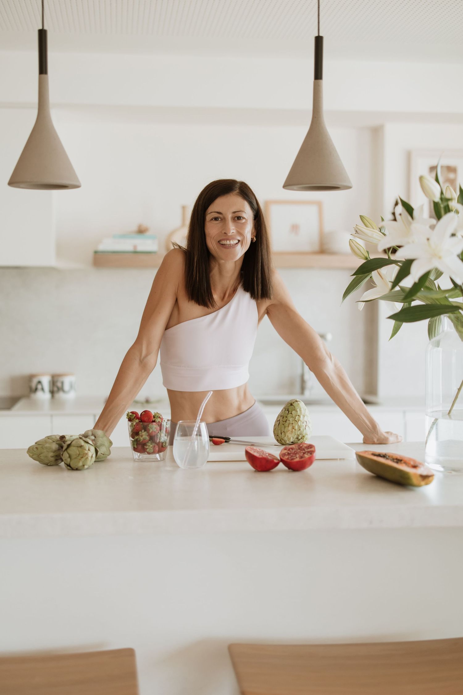 A minimalist kitchen scene with white pendant lamps and fresh produce displayed on a bright counter.
