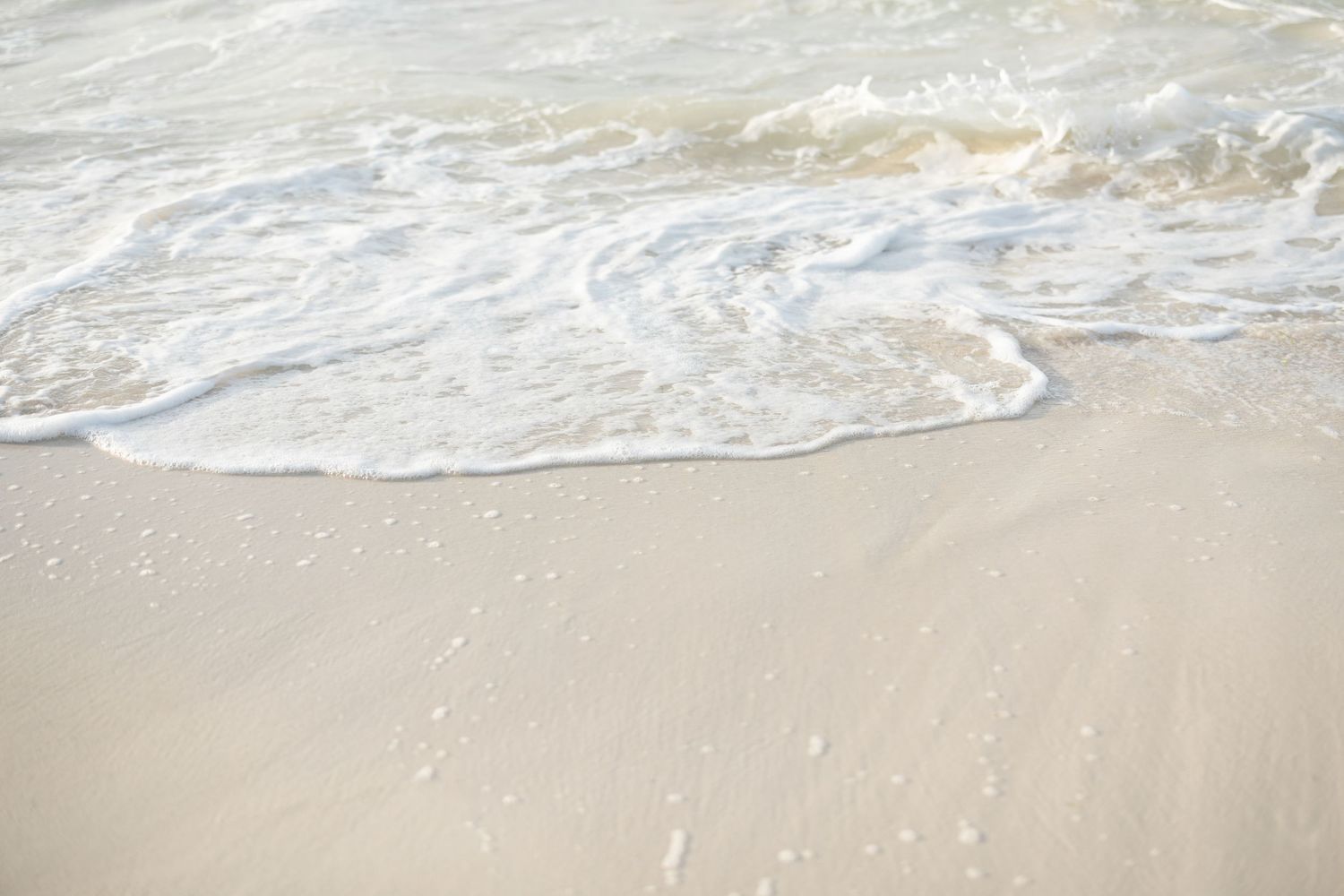 Close-up of ocean waves meeting sandy beach with foam creating natural patterns.