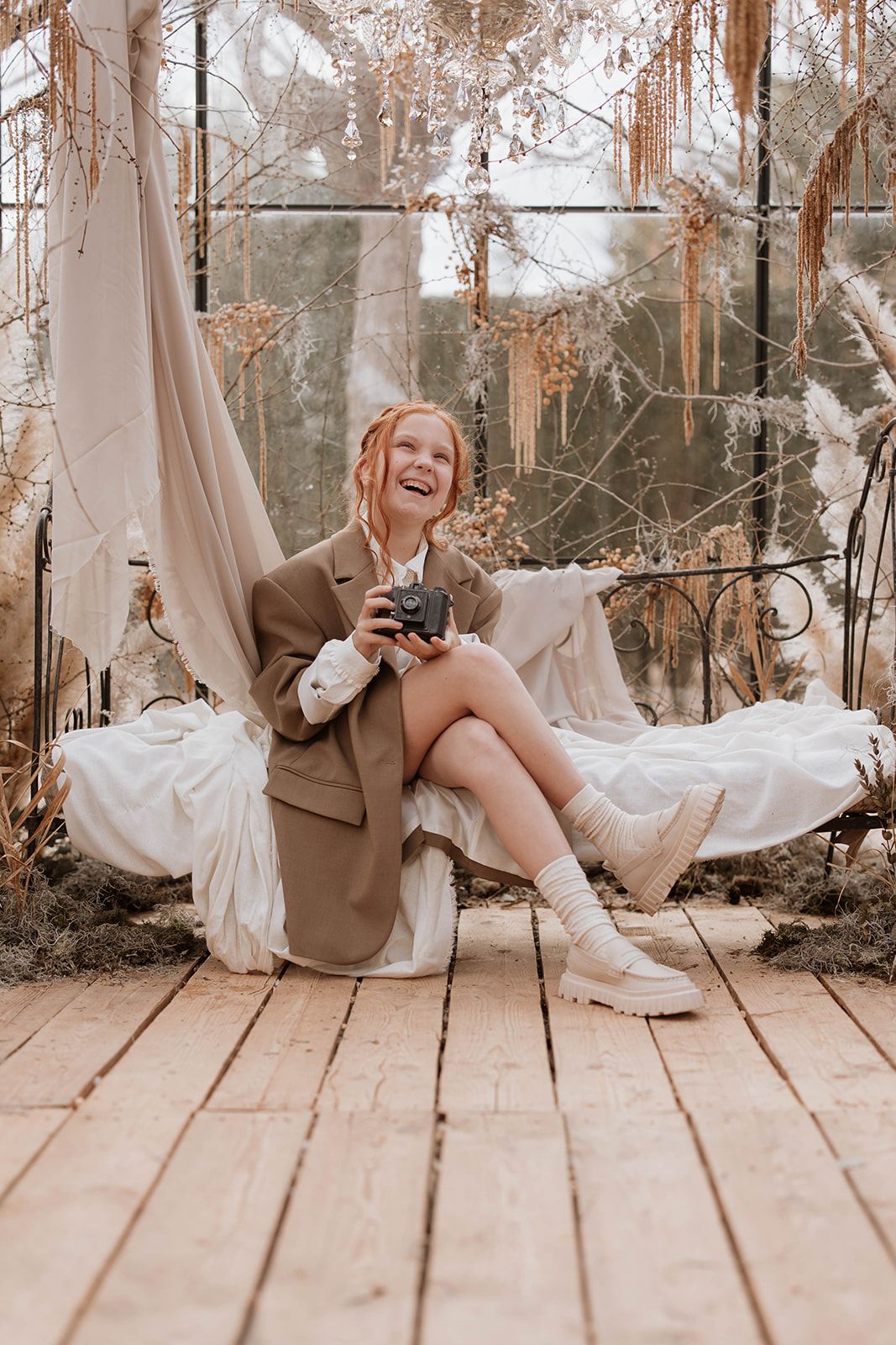 Joyful moment during greenhouse photoshoot with vintage camera and natural winter lighting.