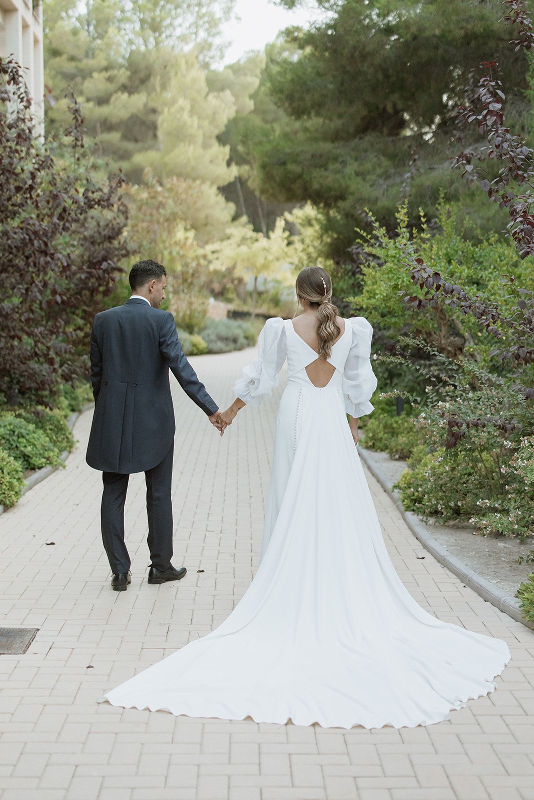 Back view of newlyweds walking down brick pathway showing full length of bride's trailing dress.