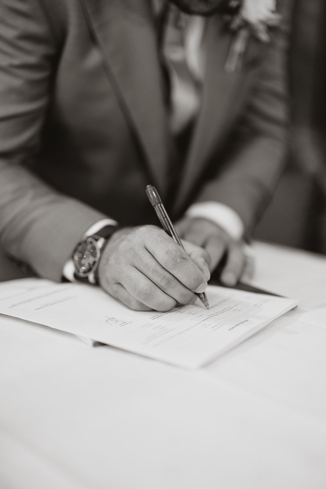 A close-up shot of hands signing a wedding document in black and white.