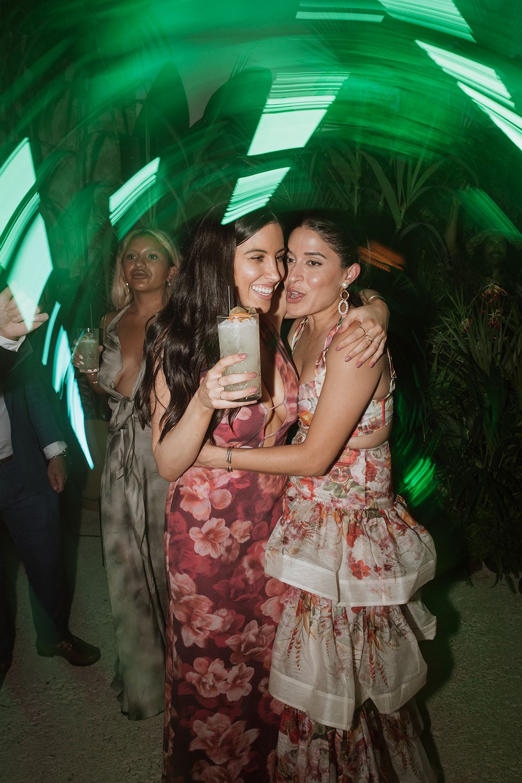 Friends celebrating under green lighting at wedding reception.
