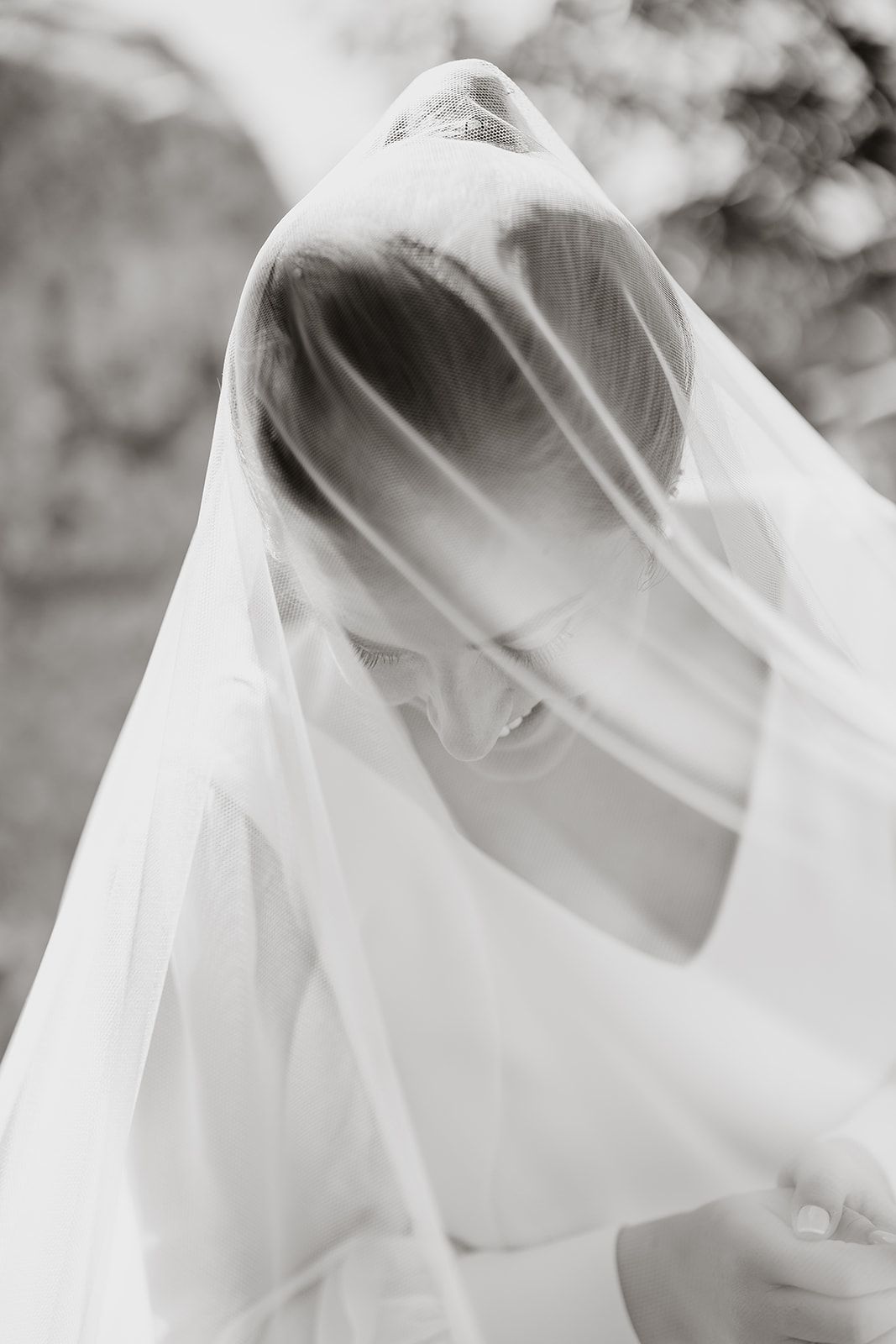 Artistic black and white portrait of bride veiled in ethereal light.
