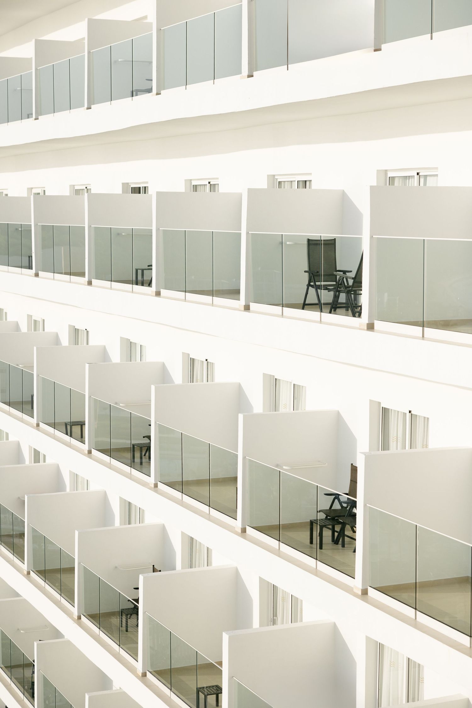 Minimalist white hotel balconies with glass railings in geometric pattern.