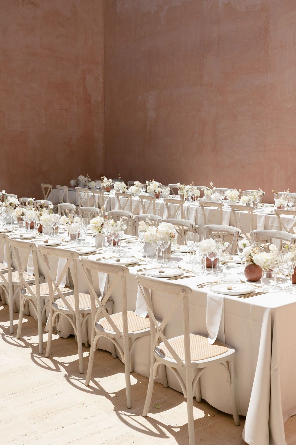 Wedding reception tables set with white linens and floral centerpieces casting dramatic shadows.