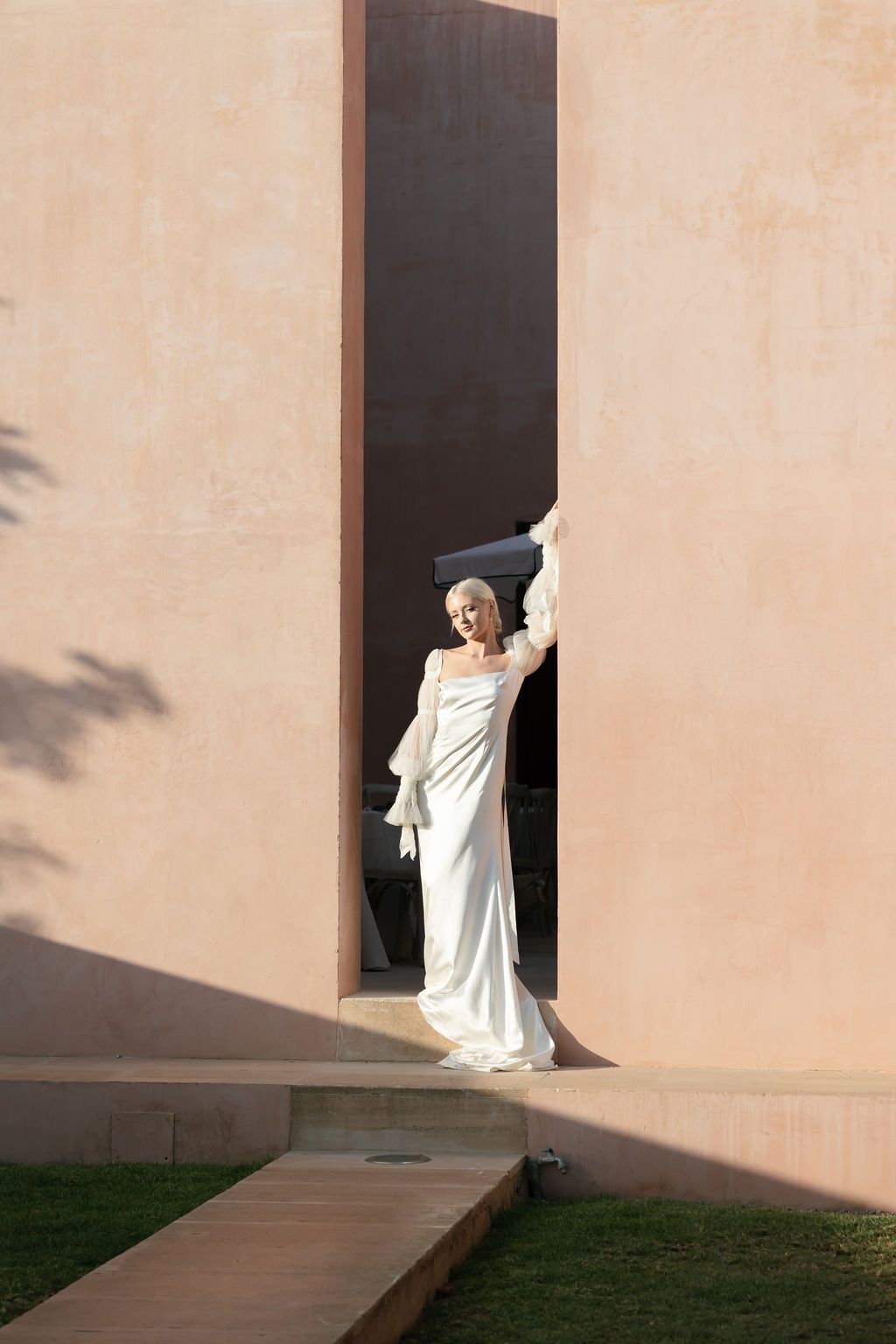 Architectural fashion photograph featuring flowing white gown framed by modern building elements.