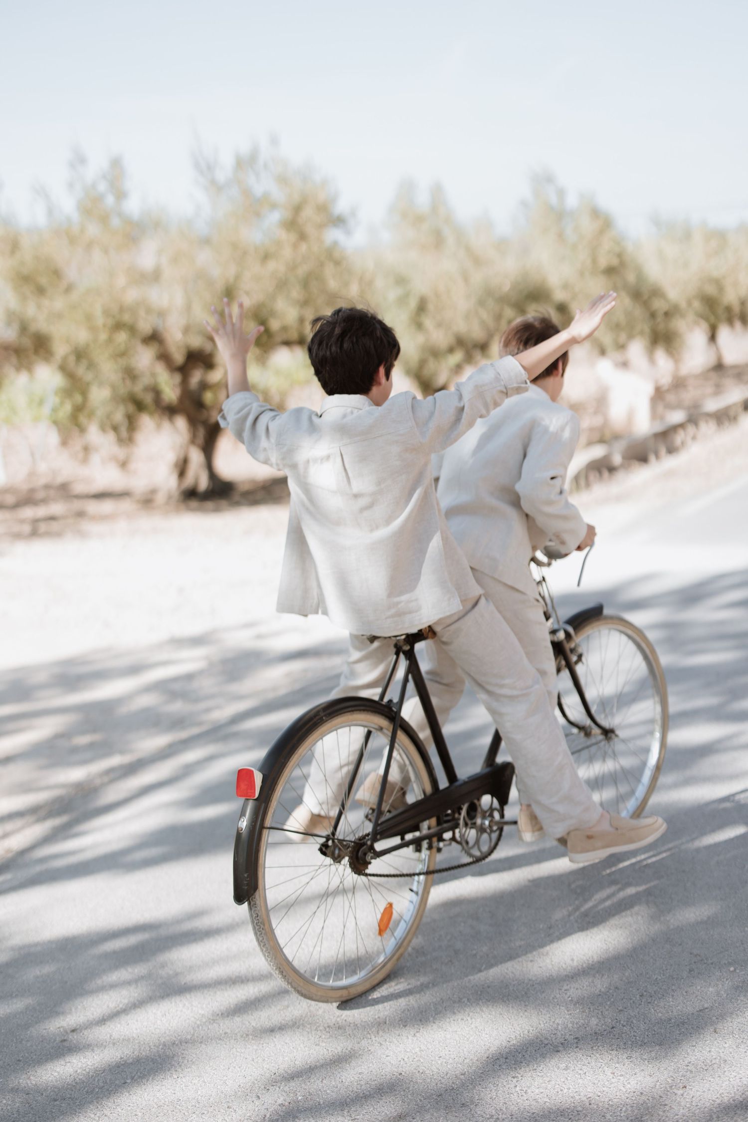 A person wearing all white flowing clothing rides a vintage bicycle on a sunny desert path.
