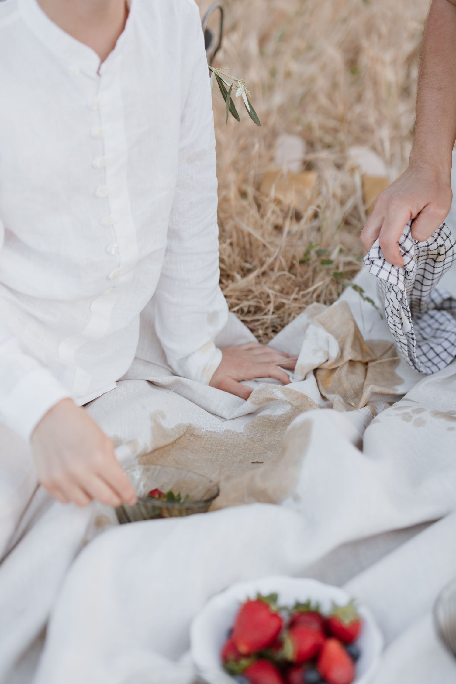 Outdoor picnic scene with white linen clothing, fresh strawberries on a plate and relaxed summer atmosphere.