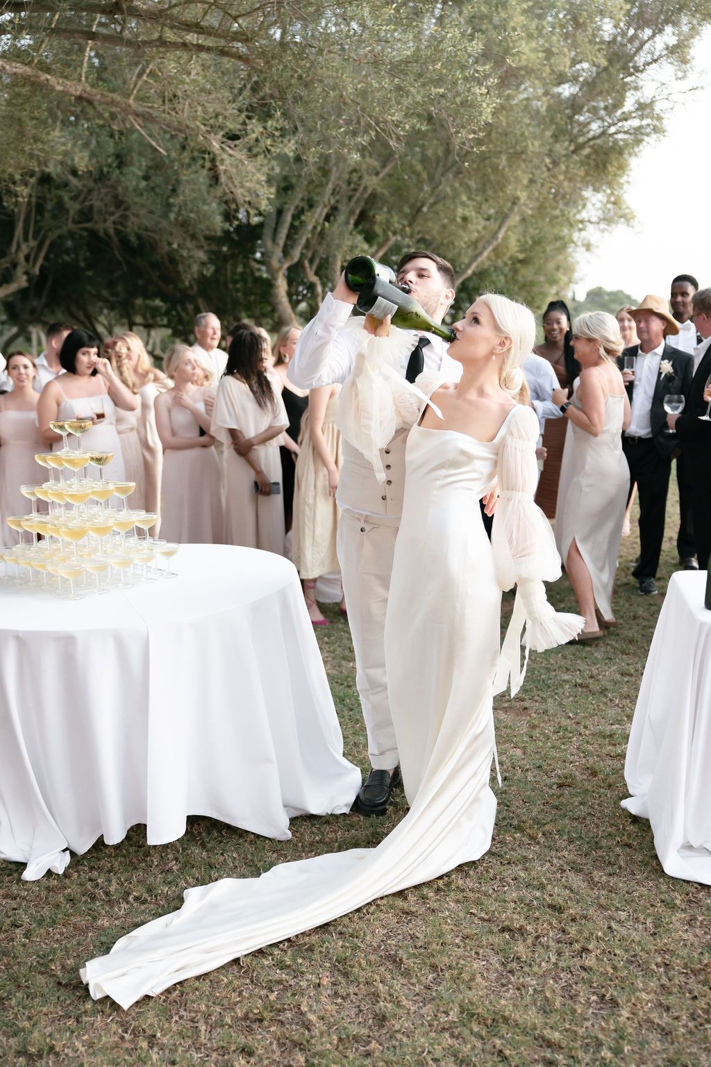 Wedding party celebrating with champagne outdoors beside an elegant glass tower display.