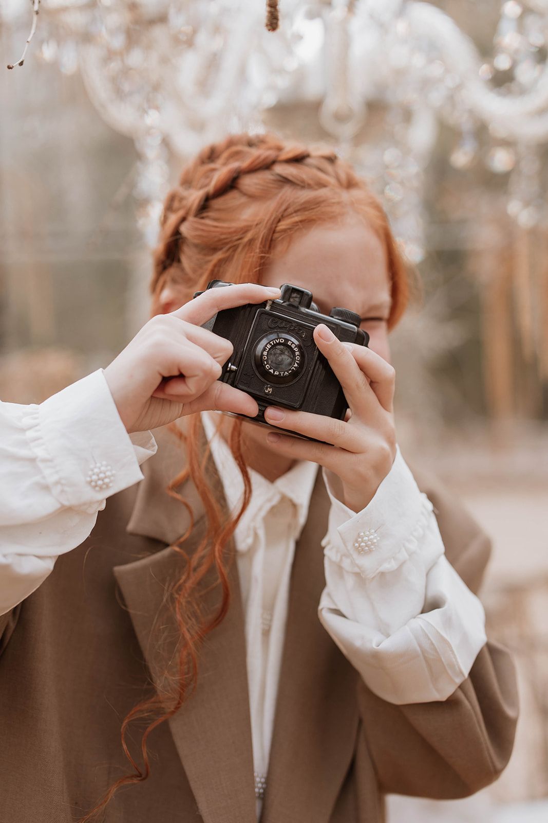 Close-up shot of hands holding vintage camera with autumn-toned background and crystal decorations.