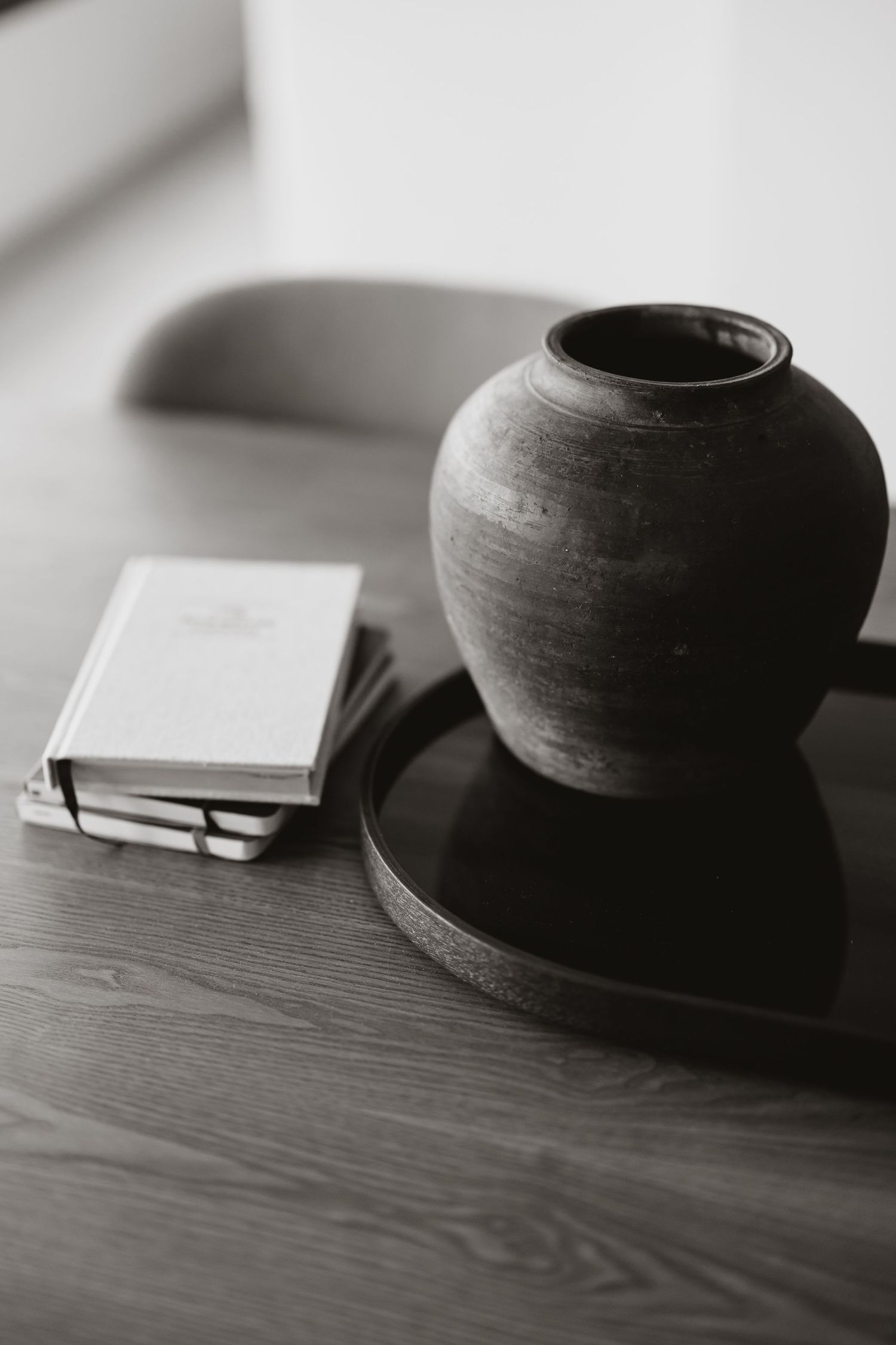 A clay pot and book arranged on a wooden surface in monochrome style.
