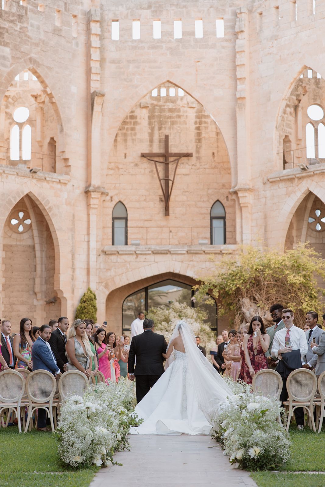 An elegant outdoor wedding ceremony setup with white floral arrangements against historic stone architecture.