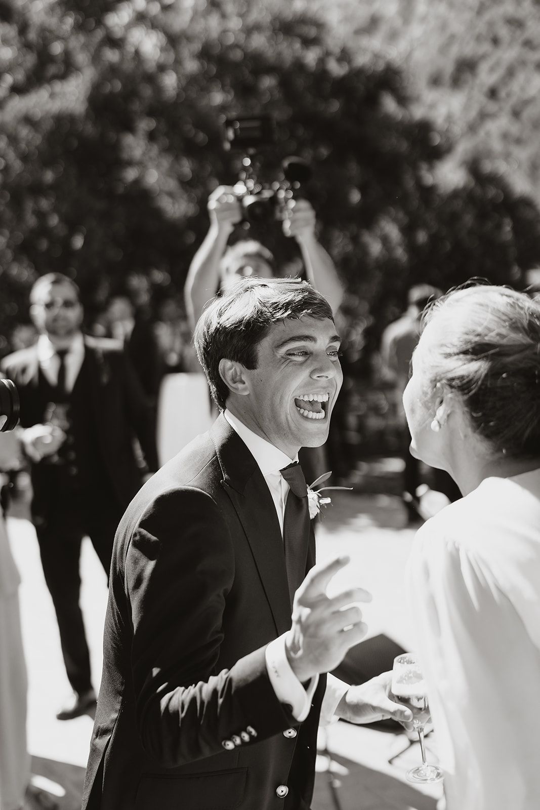 A candid black and white photo captures joyful laughter during a wedding celebration.