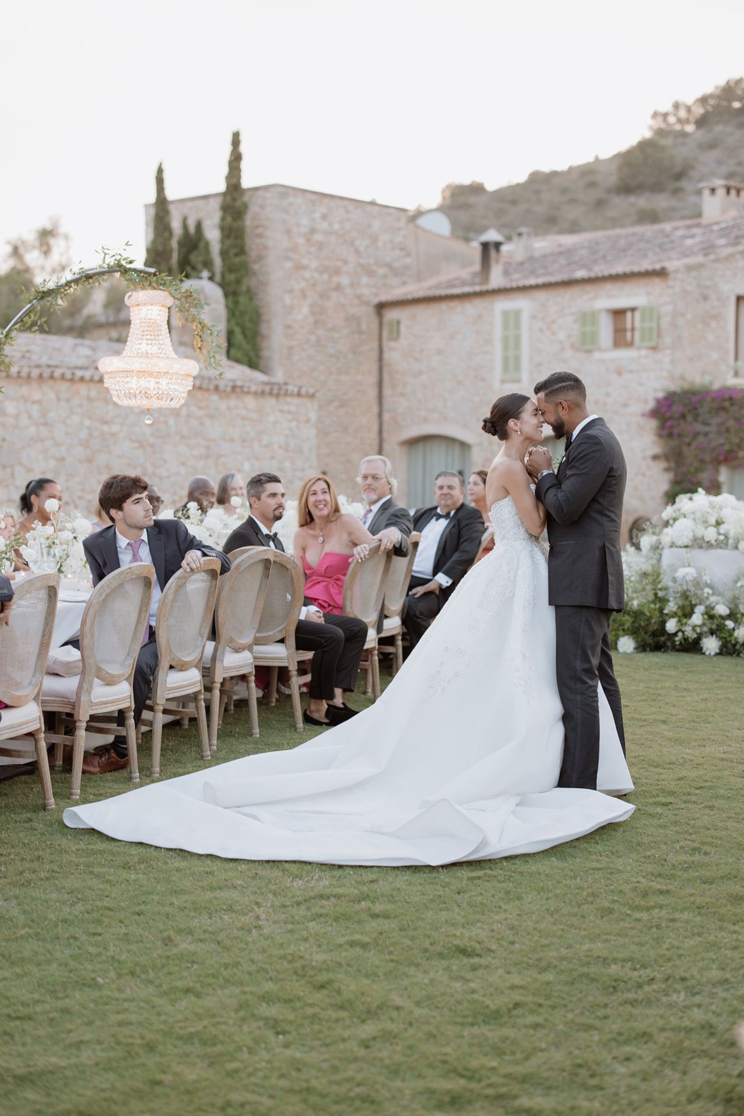 An elegant outdoor wedding ceremony with a chandelier and stone building backdrop.