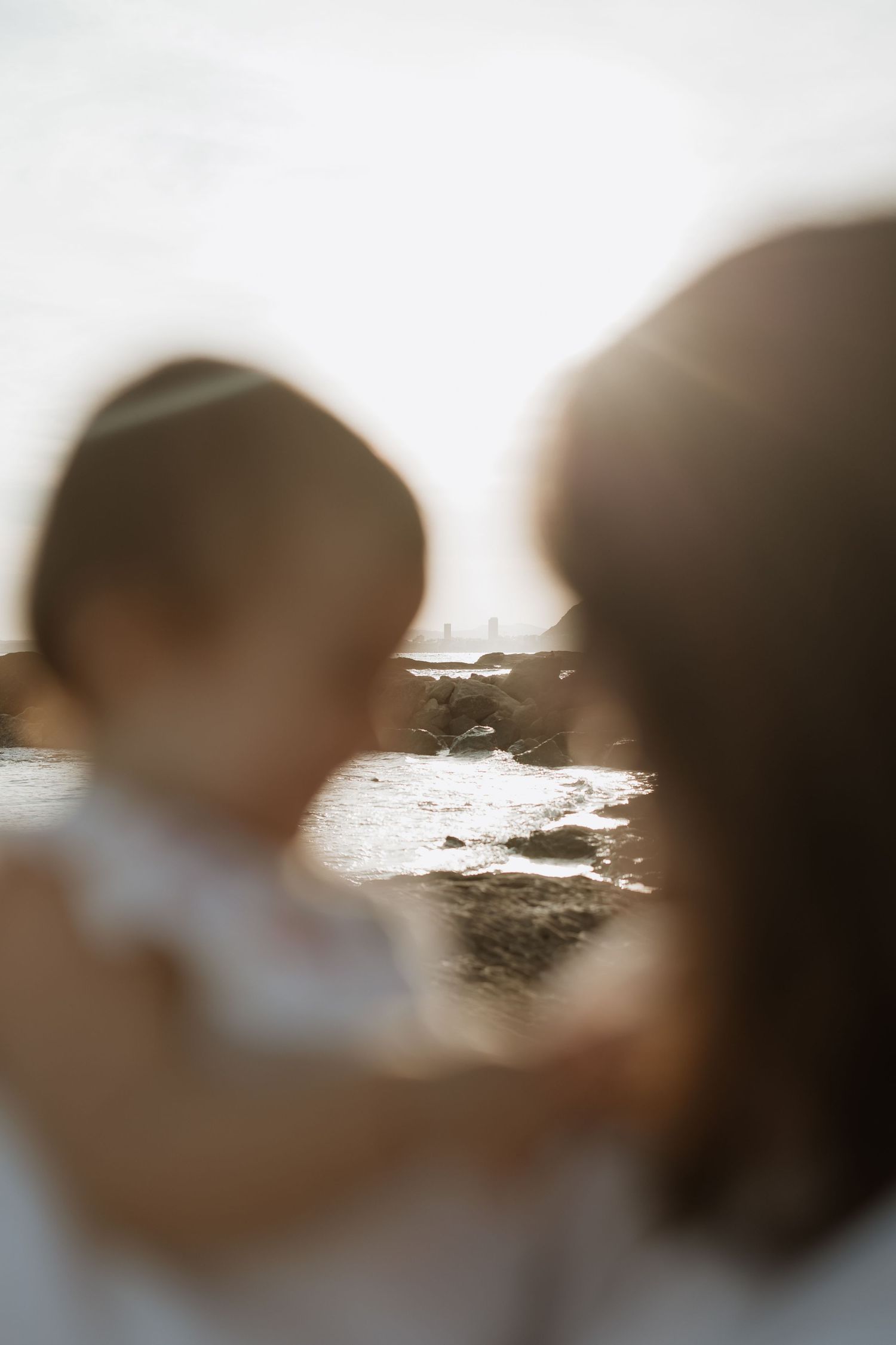A blurred silhouette portrait of figures against an ocean backdrop at sunset.
