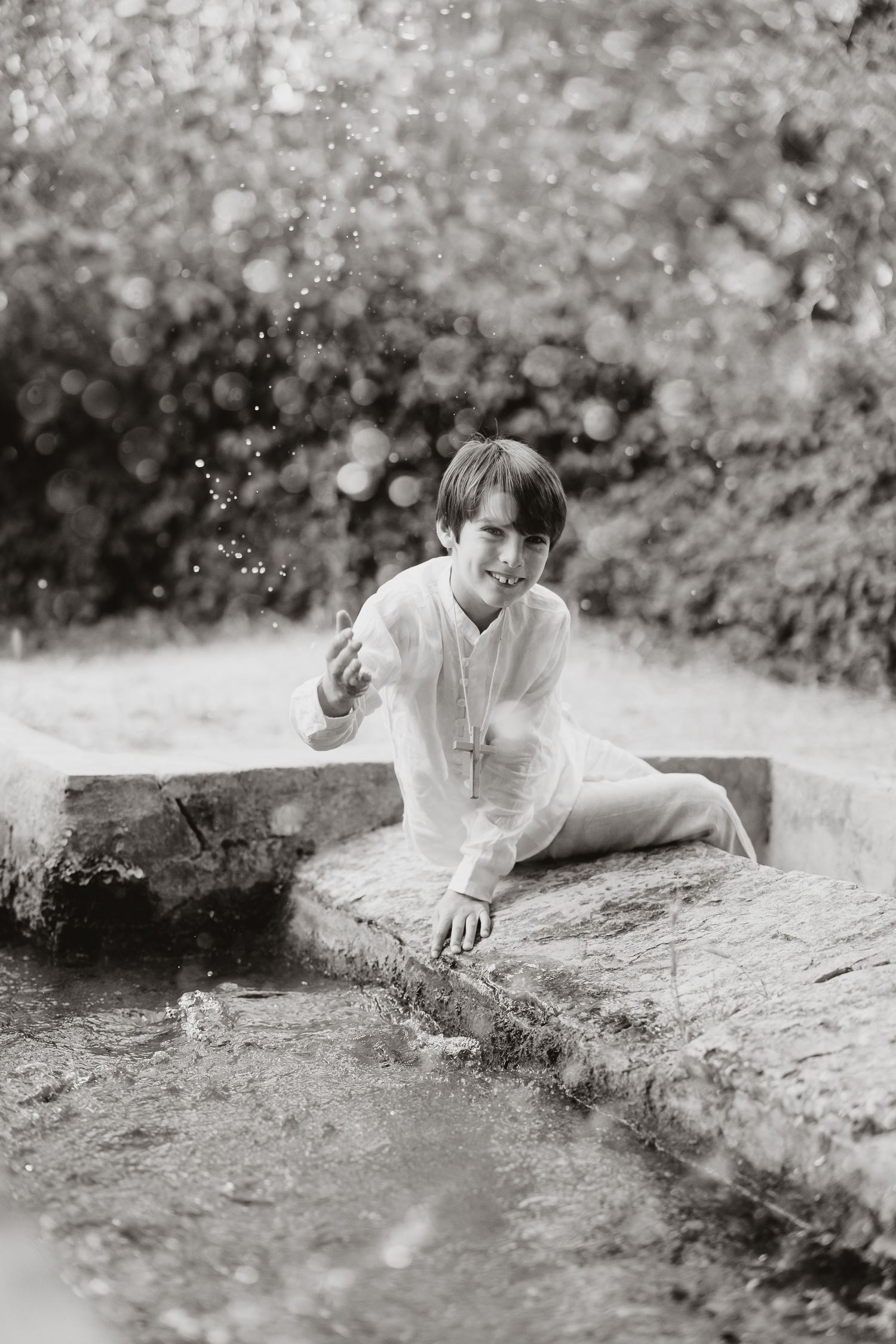 A person in a white shirt sits by a stream splashing water in a dreamy black and white vintage photograph.