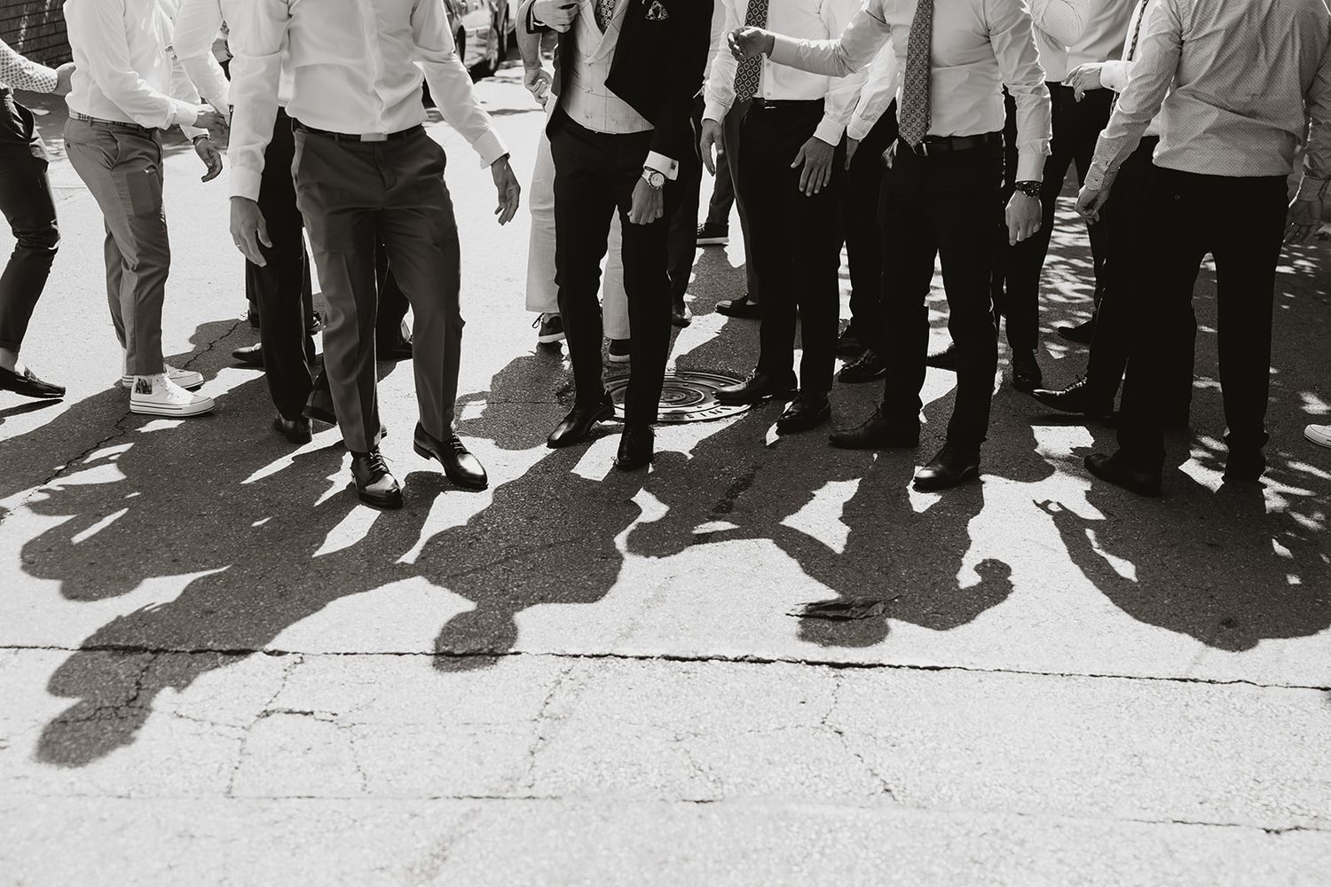 Black and white photo showing legs and shadows of groomsmen standing in a row.