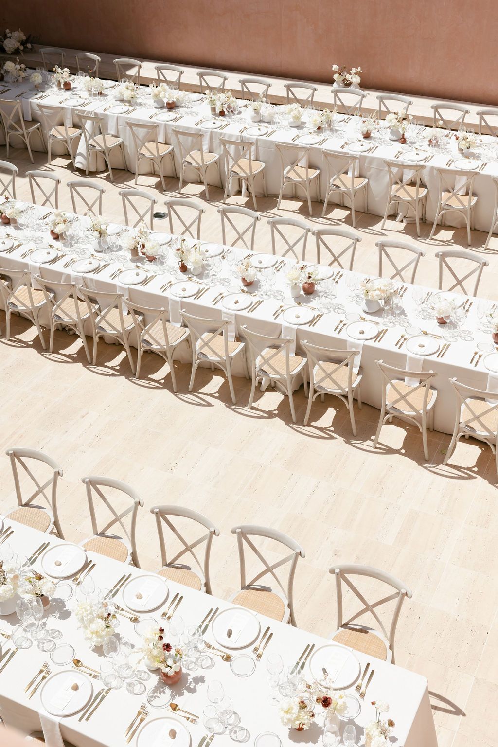 Overhead view of white wedding tables with cross-back chairs creating geometric patterns.