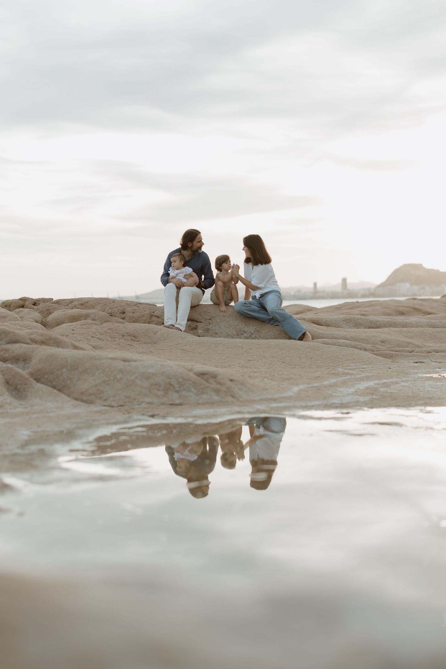 Family gathering on rocky shore with mountains and water reflections.