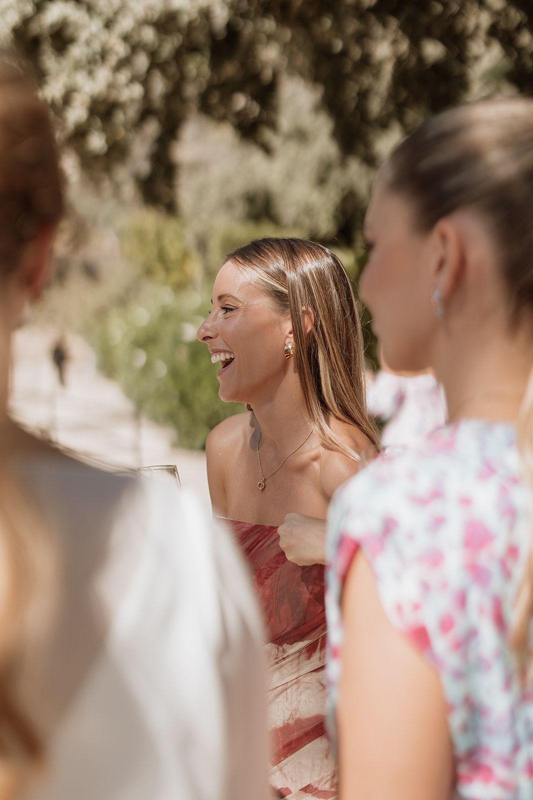 Wedding guest in red dress laughing during outdoor celebration.
