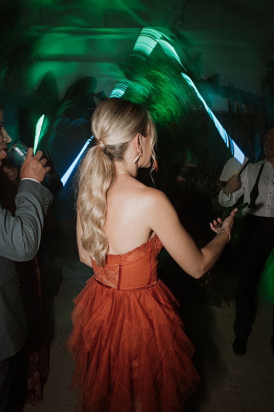 Woman in coral dress dancing under green neon lights at reception party.
