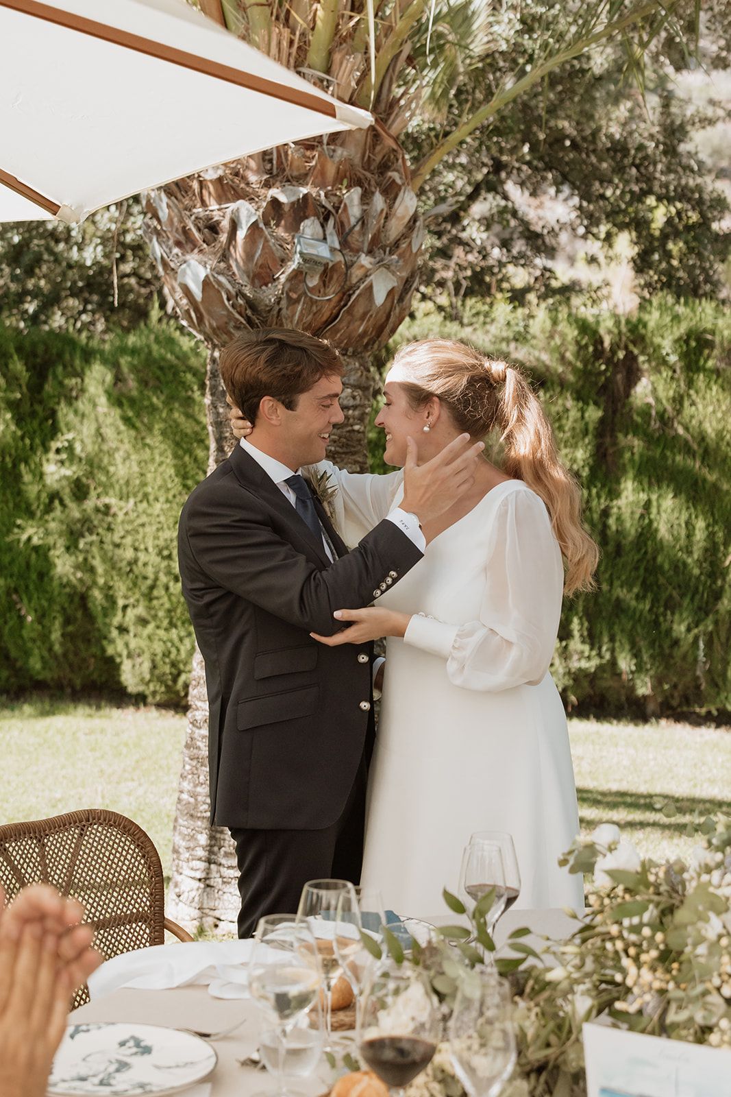 Intimate moment between newlyweds during outdoor reception under palm trees.
