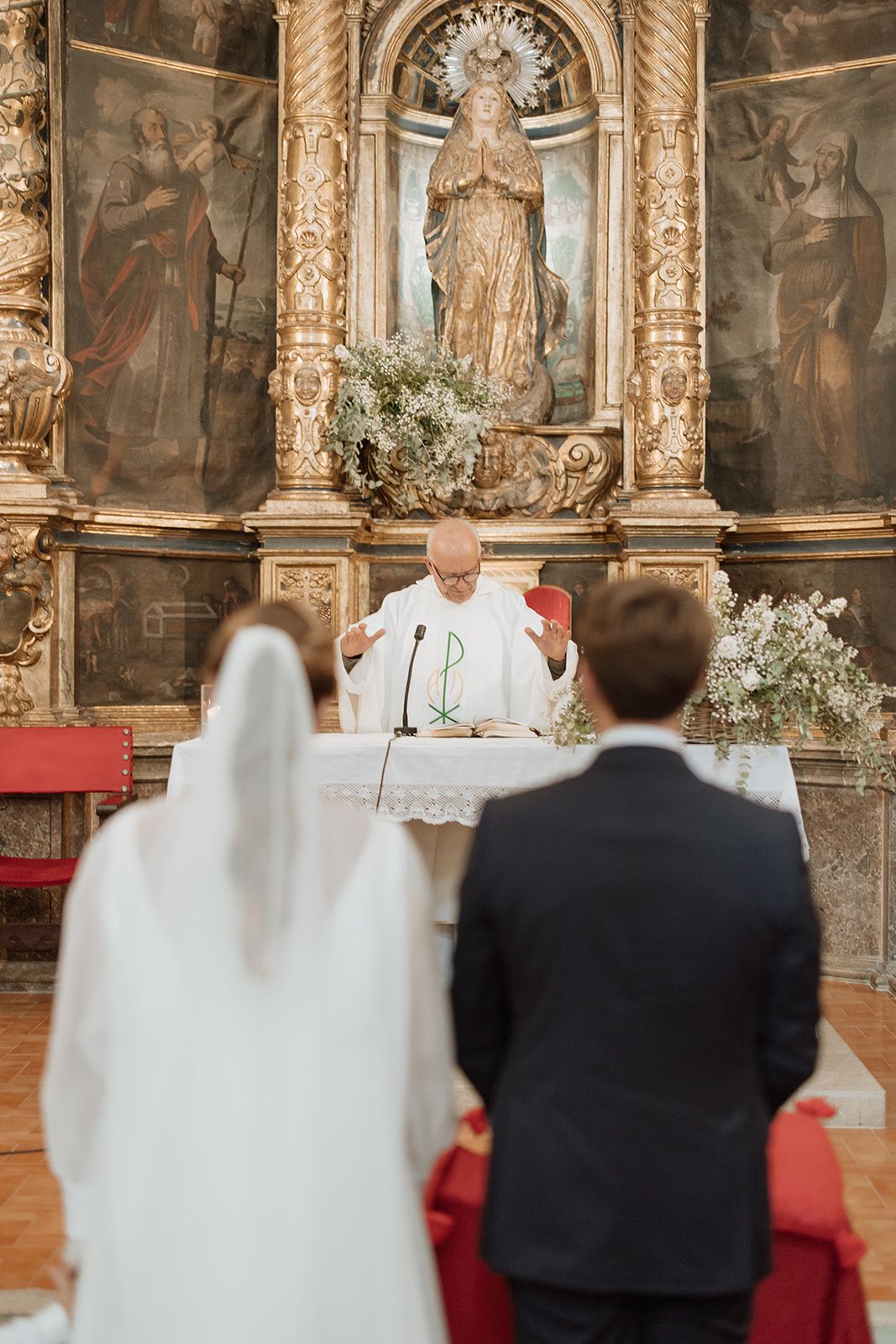 A couple stands before a priest at the altar during their Catholic wedding ceremony.