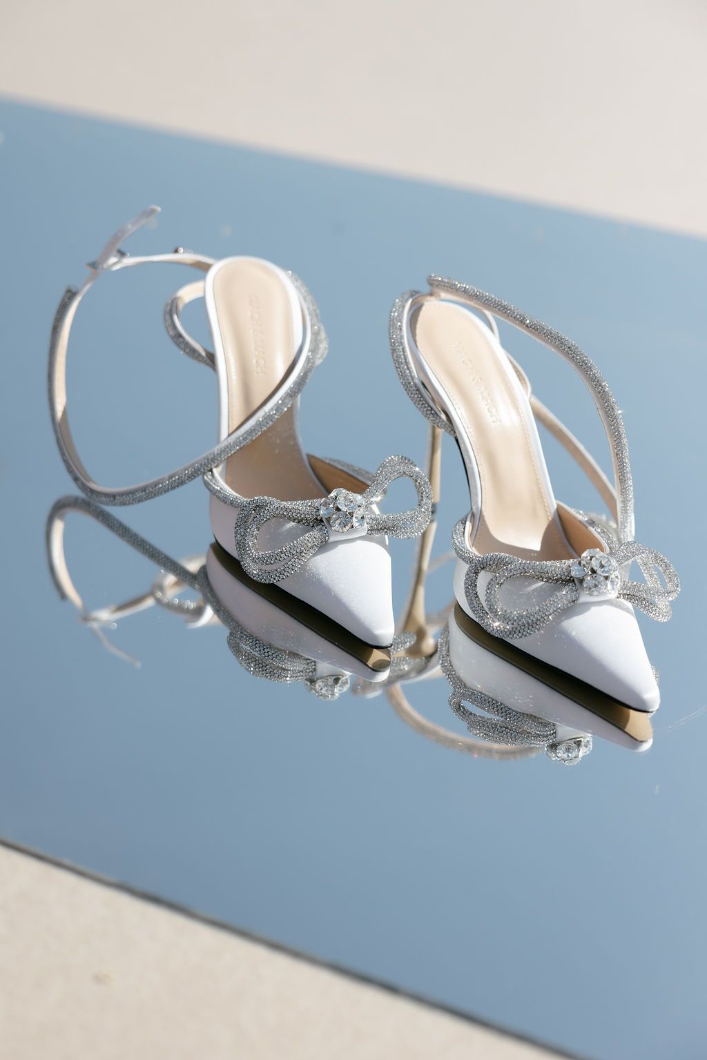Silver bridal sandals arranged in artistic composition against blue background.