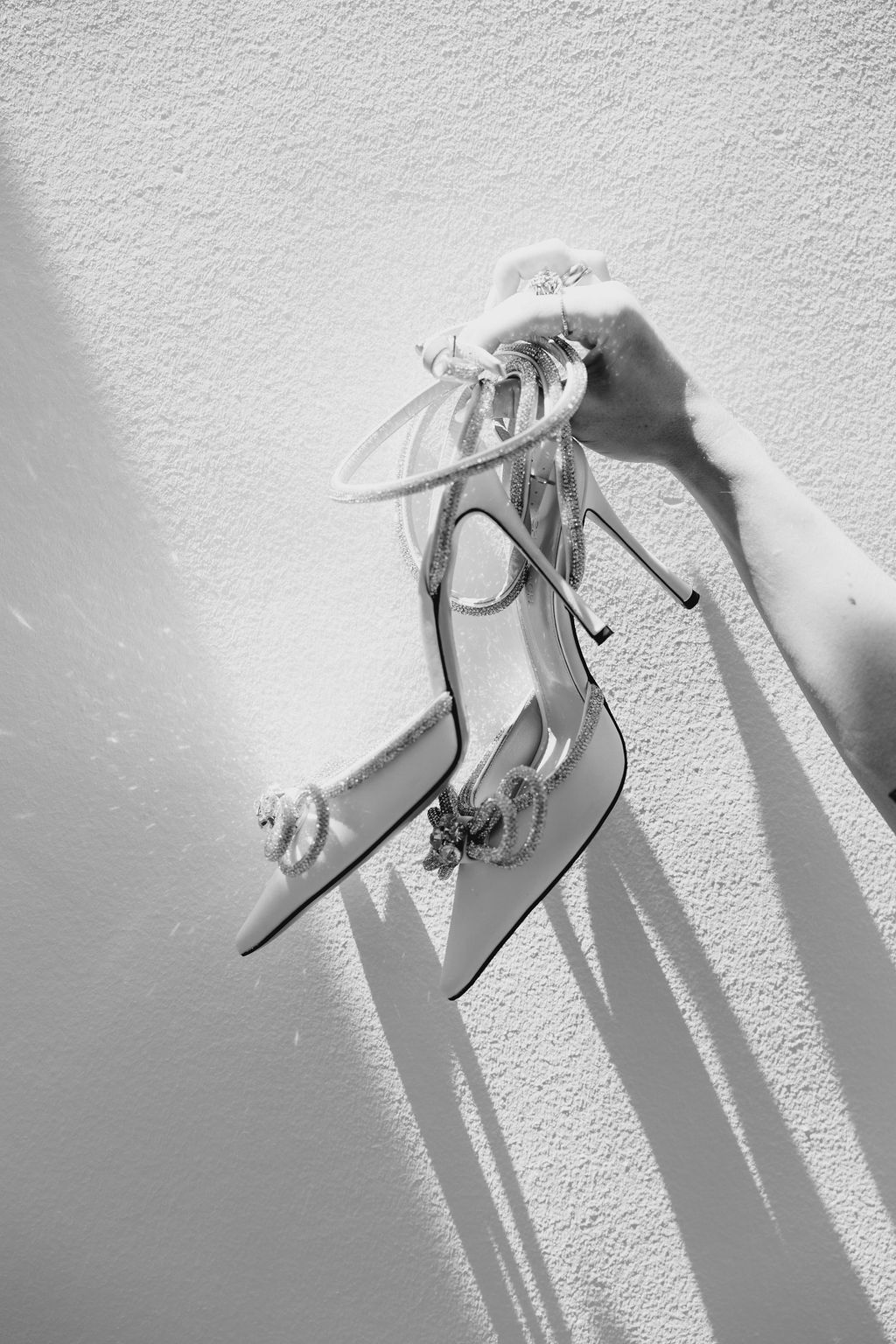 An elegant white bridal heel shoe casting dramatic shadows against a light wall.