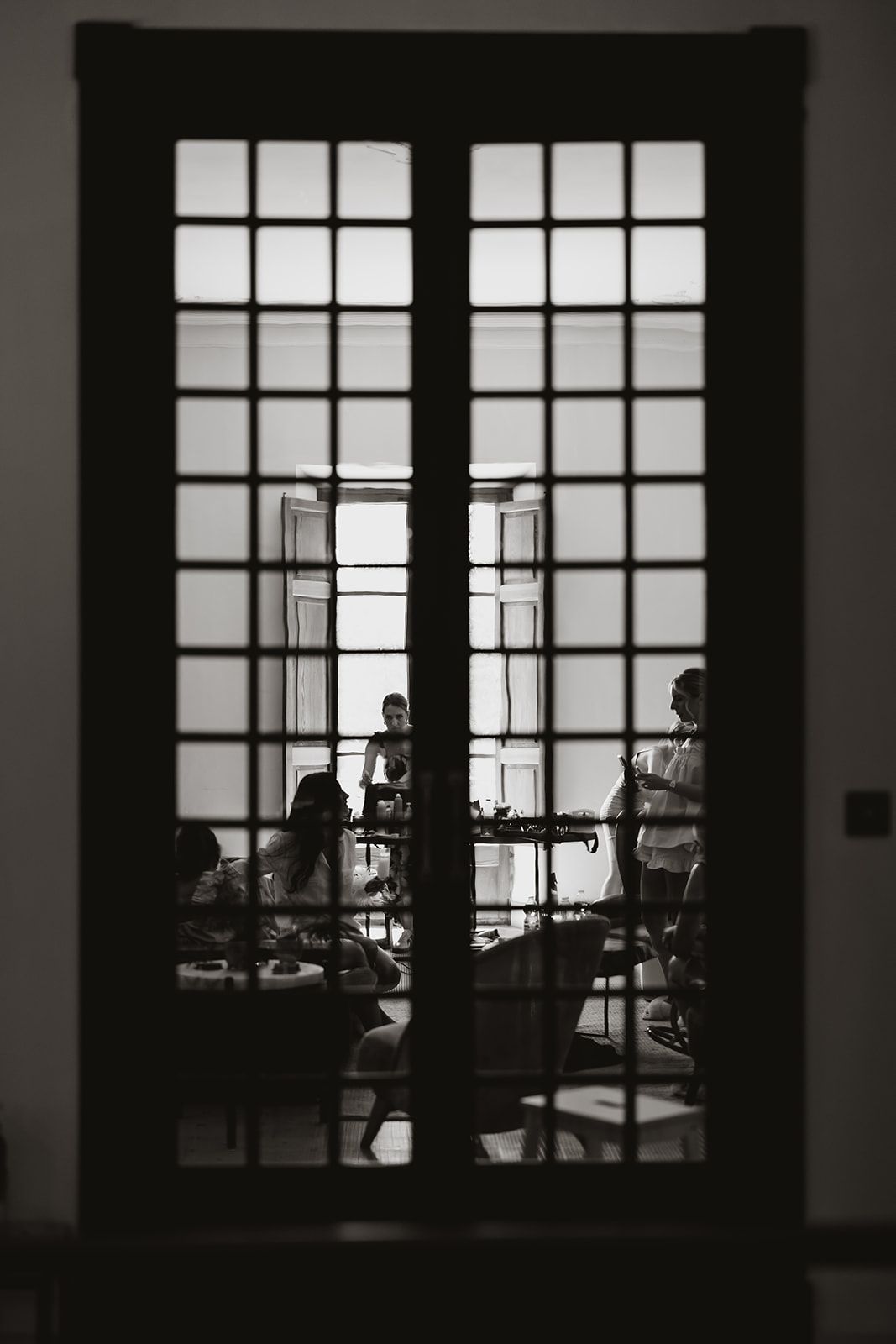 Silhouettes of people seen through gridded window panels in dramatic lighting.