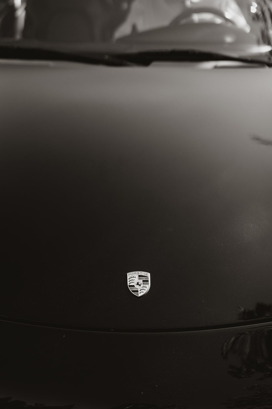 Close-up black and white detail of a Porsche badge on a car hood.