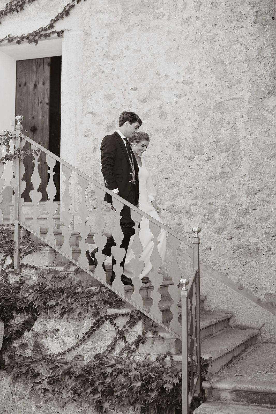 Couple descending stone stairs at a rustic venue with white stone walls.