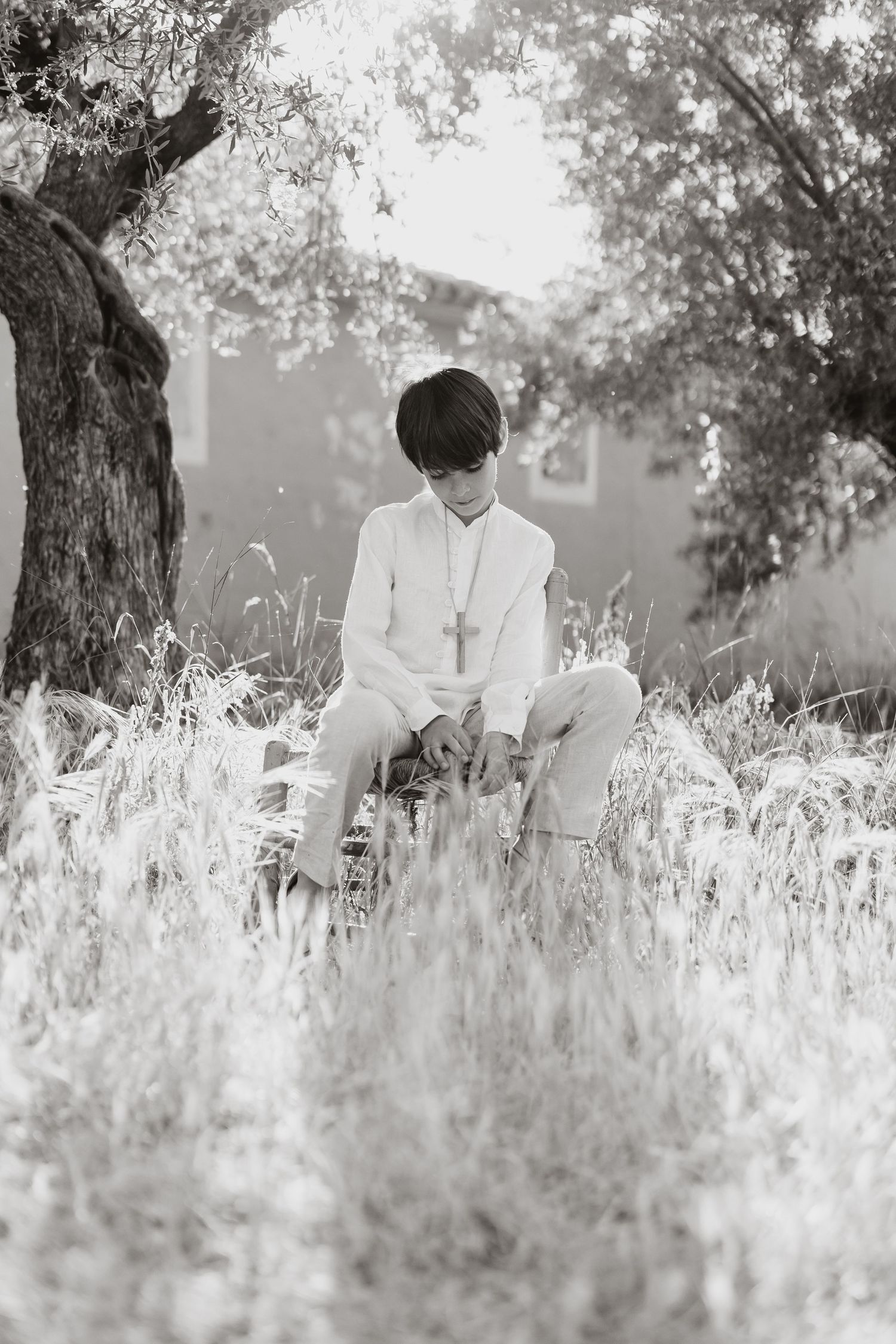 A couple in white sits together on grass beneath a tree in rustic black and white photography.