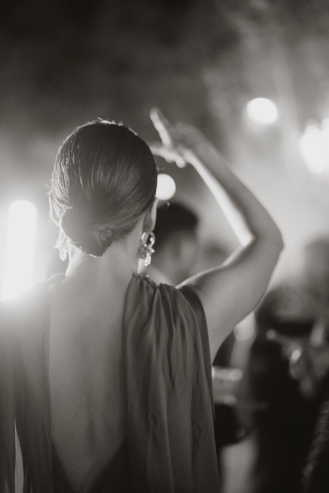 Silhouette of a woman dancing with her arm raised in backlit party lighting.