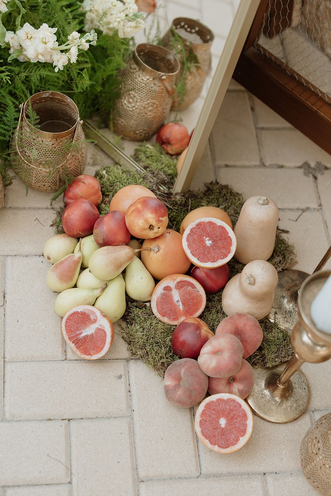 Decorative arrangement of citrus fruits, apples, and vintage lanterns on stone floor.