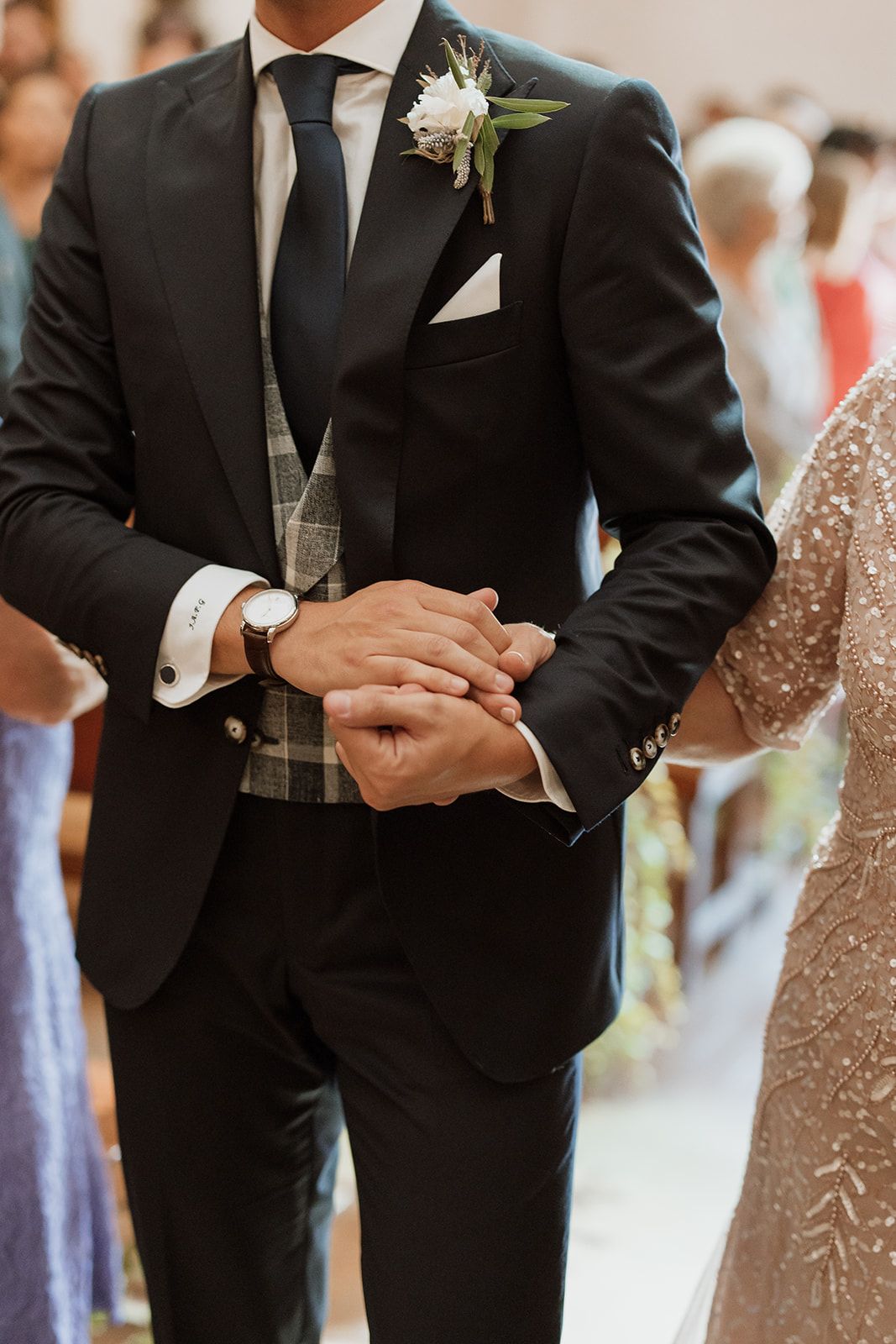 Close-up of groom's formal attire with white boutonniere and checkered vest.