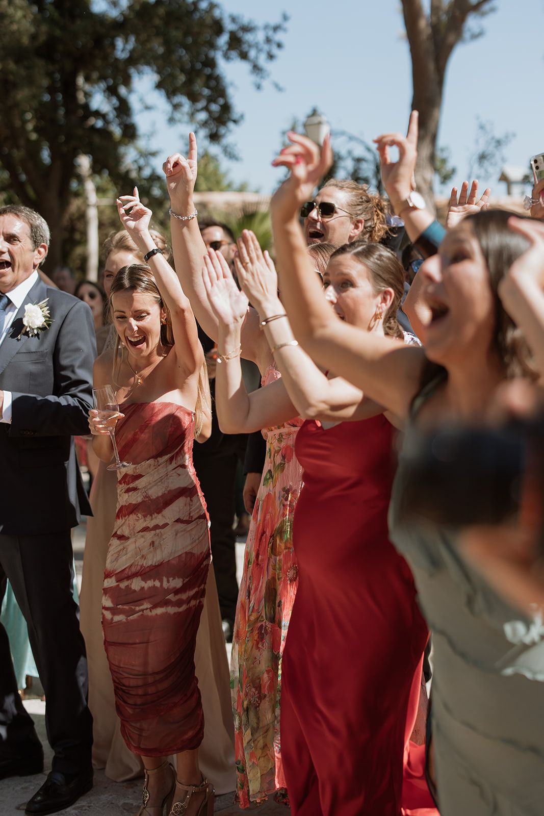 Wedding guests cheering and raising hands during outdoor celebration.
