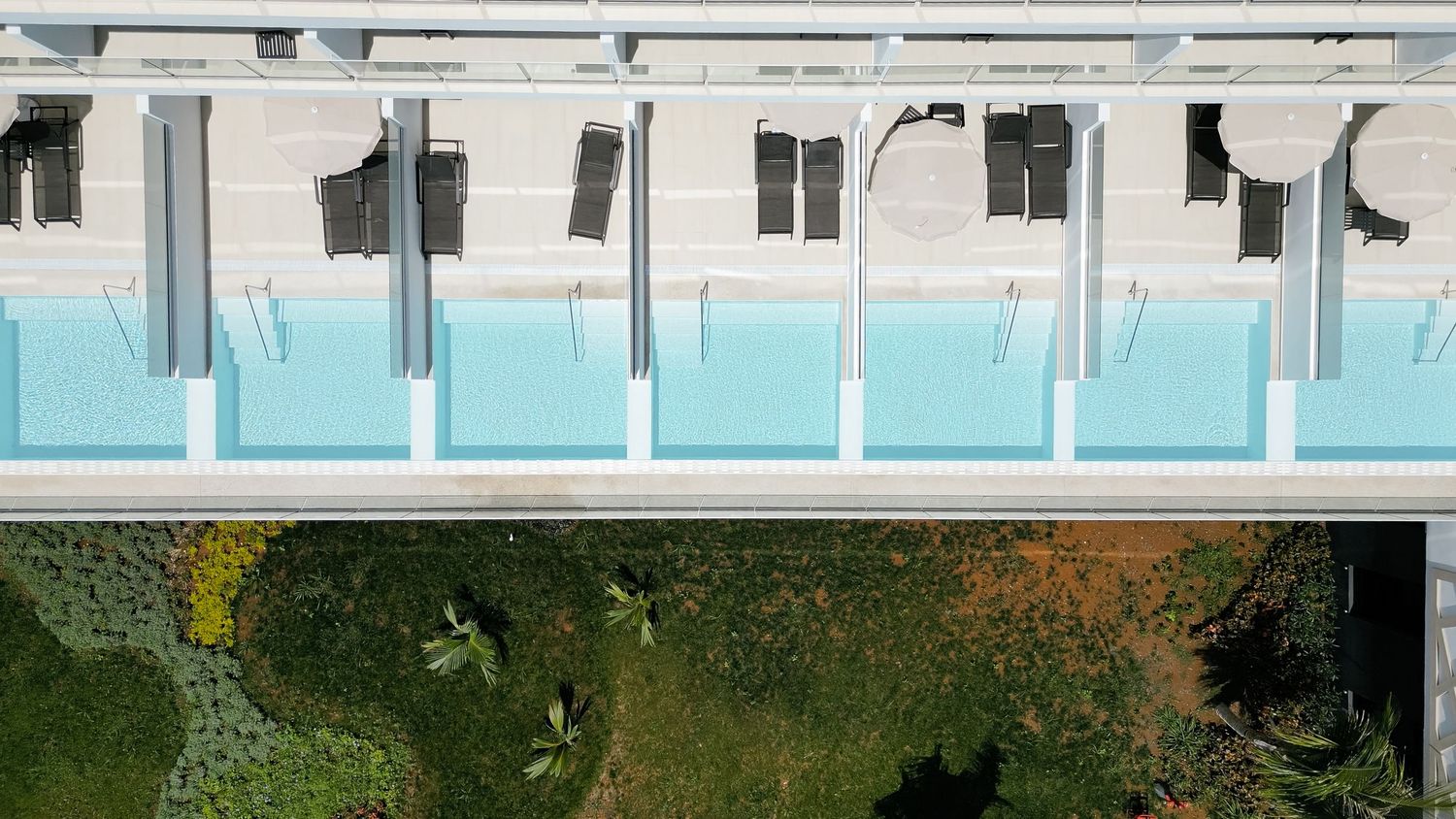 Aerial view showing a row of geometric turquoise pools on a modern building structure.