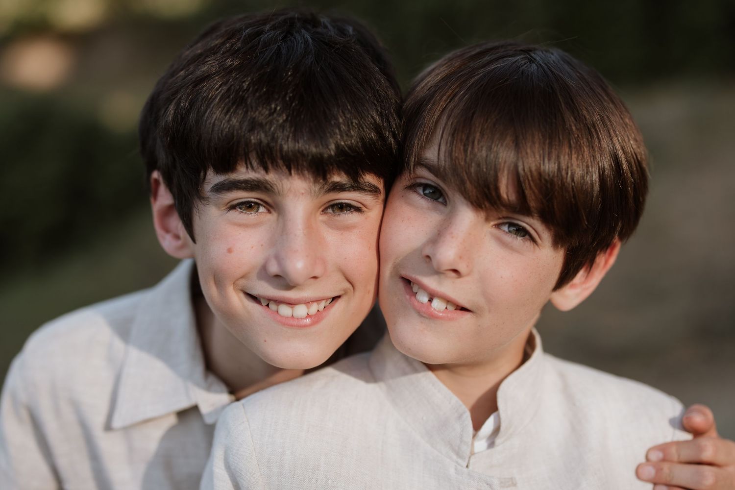 Two smiling people with brown hair in white tops embrace while posing together outdoors in soft lighting.
