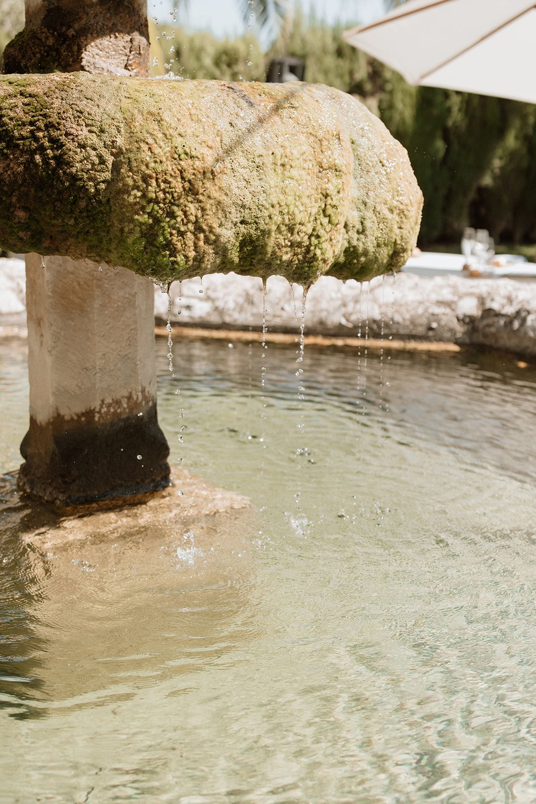 Water flows from a moss-covered stone fountain into a clear pool.